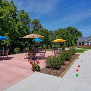A serene outdoor patio with tables, umbrellas, and a bocce court surrounded by lush greenery.
