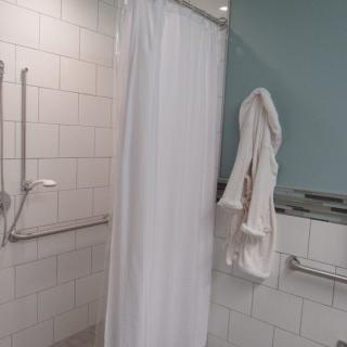 A bathroom featuring a shower with a white curtain, tiled walls, and safety handrails.