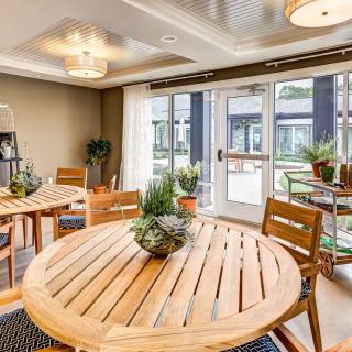 A modern dining area featuring wooden round tables, potted plants, and ample natural lighting.