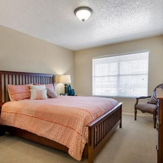 A cozy bedroom with a wooden bed, bedside lamp, and a window letting in natural light.