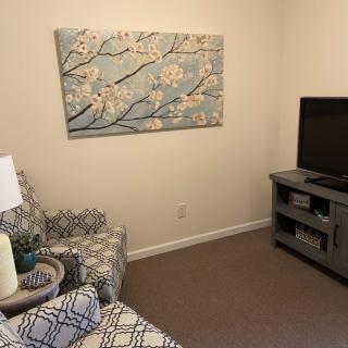 A cozy living room with patterned armchair, wall art, and a television on a stand.