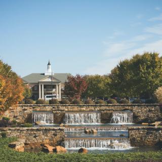 A picturesque garden scene featuring a multi-tiered stone waterfall with autumn foliage in the background.