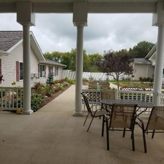 A covered patio with outdoor seating overlooking a landscaped garden area between residential buildings.