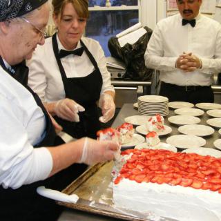 Chefs preparing a strawberry cake in a kitchen setting.
