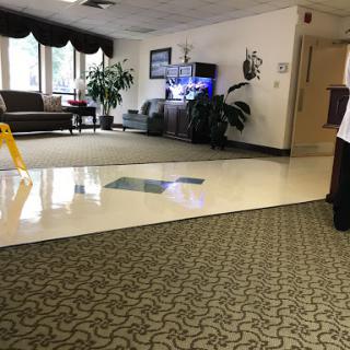 A spacious indoor lobby with seating, plants, and a television, featuring caution signage on the floor.