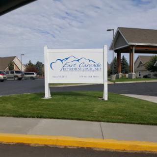 A sign indicating a location, surrounded by landscaped areas and parked vehicles.