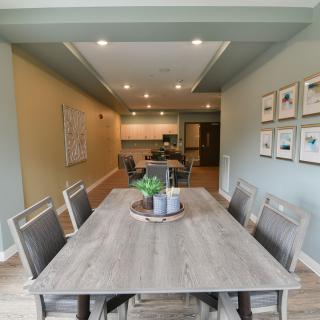 A modern dining room with a view into the kitchen, featuring a stylish table and chairs set, tasteful decor, and ambient lighting.