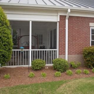 A brick house featuring a screened porch and well-maintained garden area.