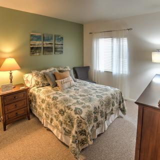 A cozy bedroom featuring a patterned bedspread, bedside tables with lamps, and wall art above the bed.