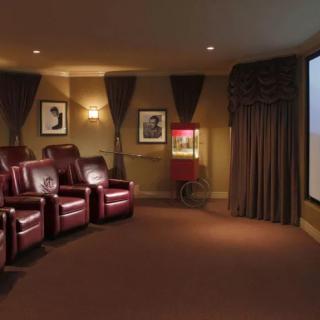 A cozy home theater with recliner chairs facing a large projector screen, complemented by warm lighting and elegant wall art.