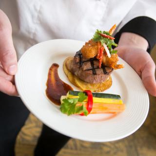 A chef presents a gourmet dish featuring steak and vibrant vegetables, artfully arranged on a white plate.