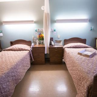 A clean hospital room with two single beds, bedside tables, and soft lighting.