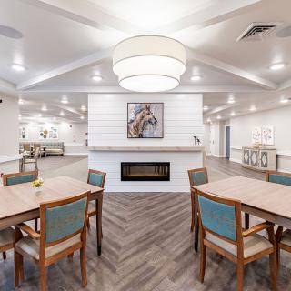 A modern dining area featuring multiple tables and chairs, a central fireplace, and contemporary lighting.