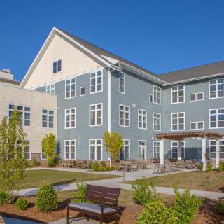 A modern residential building with a landscaped garden and benches in the foreground.