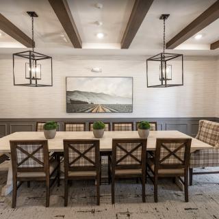 A stylish dining room featuring a wooden table surrounded by chairs, accented with hanging lights and ceiling beams, complemented by wall art and small plants.