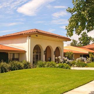 A sunny view of a building with arched windows, surrounded by a green lawn and trees.