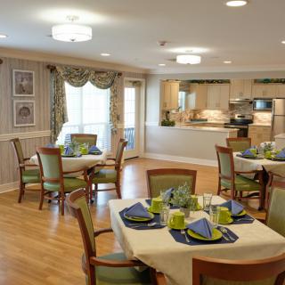 Elegant dining room with neatly arranged tables and chairs, featuring a view into an open kitchen area.