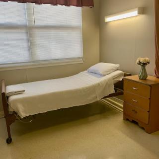 A hospital room featuring a bed, bedside table, and natural light from the window.