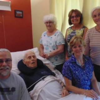 Family gathered around an elderly man in a hospital bed.