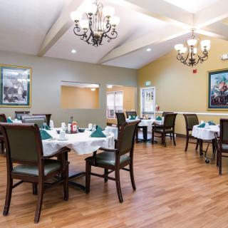 A well-lit dining area with elegant chandeliers and neatly arranged tables and chairs.