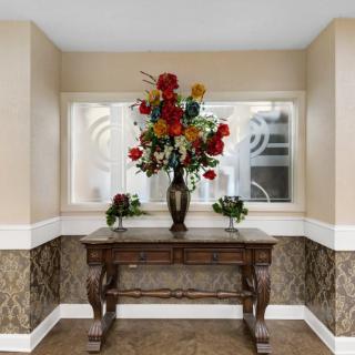 A decorative table with a flower arrangement in front of a window.