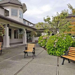 A spacious courtyard with benches and surrounding greenery in front of a house.