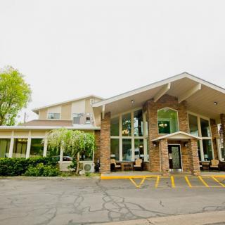A modern hotel building featuring large windows and a welcoming entrance, surrounded by greenery.