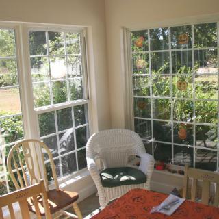A cozy sunroom with large windows letting in natural light, featuring a wicker chair and a wooden table surrounded by chairs.