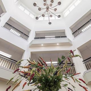A modern atrium with multiple balconies, featuring a central chandelier and decorative plants.