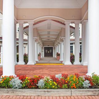 A symmetrical architectural entrance with white columns and vibrant flower beds.
