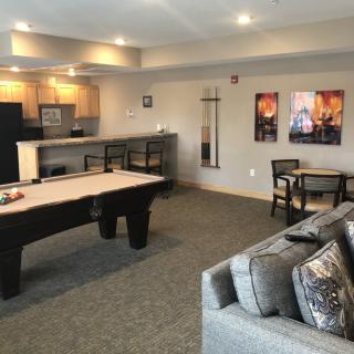 A modern game room featuring a shuffleboard table, kitchenette, and comfortable seating.