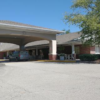 A view of a commercial building with a covered entrance and parked vehicles on a sunny day.