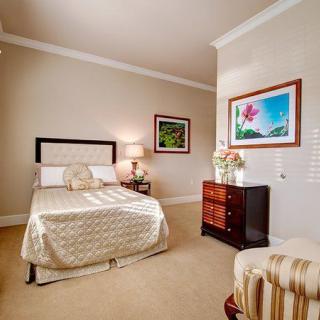 A cozy and elegantly decorated bedroom featuring a bed, side table with a lamp, artwork on the walls, and patterned textiles.