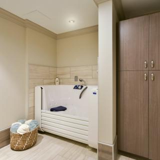 A modern bathroom with an accessible bathtub, storage cabinet, and a basket of towels.