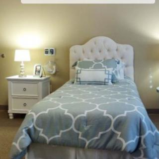 A cozy bedroom with a single bed, tufted headboard, and nightstand featuring a lamp.