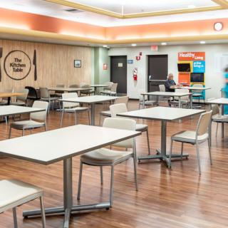 A modern cafeteria with empty tables and chairs on a wooden floor.