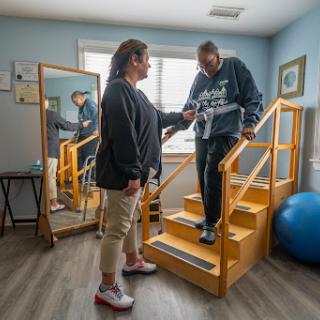 A patient receives assistance from a therapist while practicing climbing stairs in a rehabilitation setting.