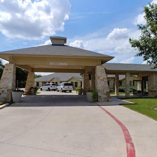 A covered entrance to a building with a driveway under a partly cloudy sky.