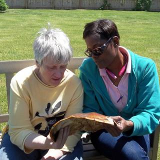 Two people sitting on a bench outside, sharing a moment as they read together.