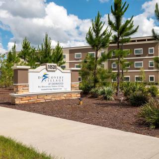 A modern building with a landscaped exterior and a prominent sign under a cloudy blue sky.