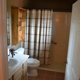 A tidy bathroom featuring a shower area, toilet, and sink with wooden storage.