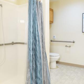An accessible bathroom with a shower, blue curtain, and a toilet equipped with grab bars.