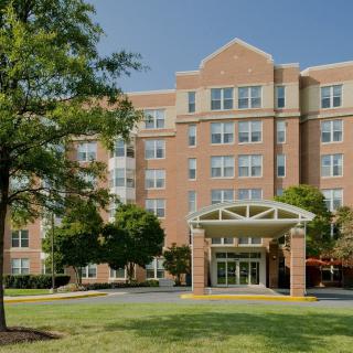 A multi-story brick residential building with a prominent entrance, surrounded by trees and greenery.