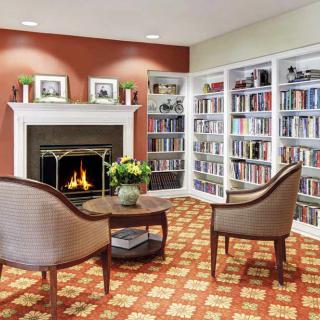 A cozy library corner with a fireplace, surrounded by bookshelves and two chairs.