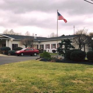A small building with an American flag flying outside, a red car parked nearby, and a cloudy sky overhead.