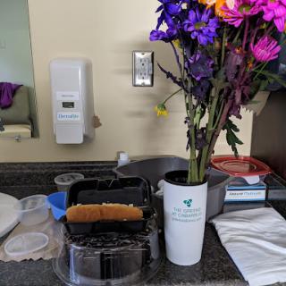 A colorful arrangement of flowers in a cup on a kitchen counter alongside food.