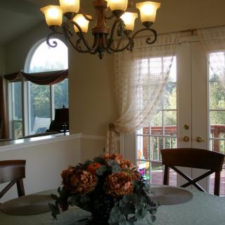 A cozy dining room with a chandelier, floral centerpiece, and large windows.