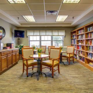 A cozy library reading area with bookshelves, tables, and chairs.