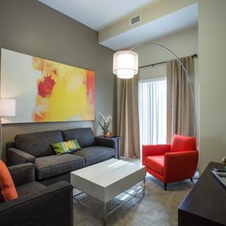 A modern living room with a dark sofa, vibrant artwork, and a red armchair.