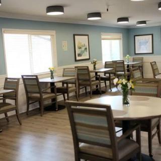 A clean and bright dining area with multiple tables and chairs arranged neatly, featuring modern decor and a wooden floor.